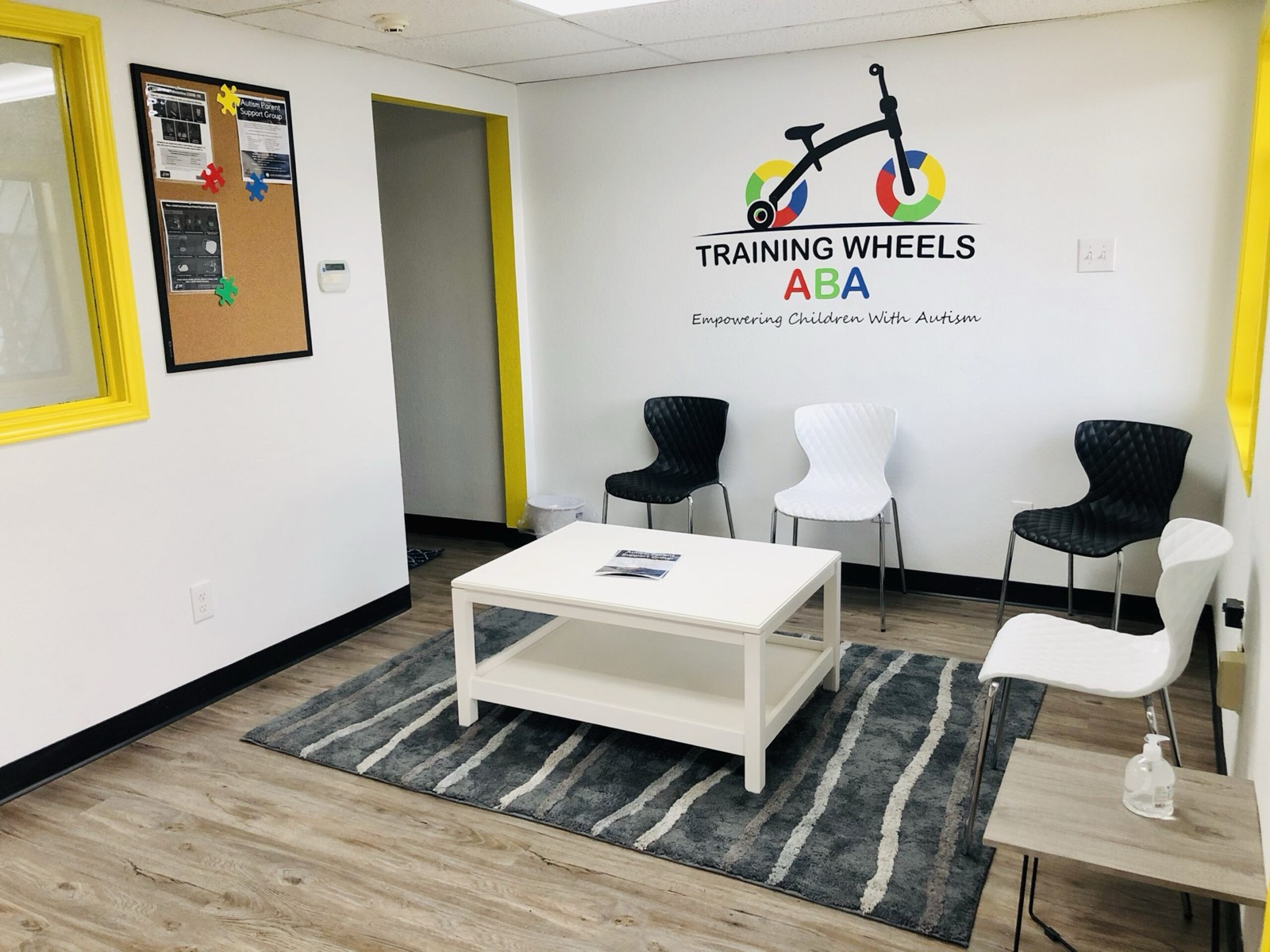 A Training Wheels ABA waiting room with the logo on the wall, chairs, and a low table